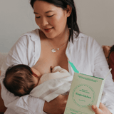 Woman breastfeeding a baby while holding a green book titled 'franjos kitchen'.