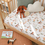 A fitted crib mattress cover with a whimsical woodland pony print, styled on a wooden crib with a plush bunny, a cloud pillow, a book, and a small toy horse.