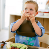 Child eating a piece of bread with a bib on, sitting at a table with food.