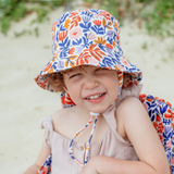Child wearing a colorful floral bucket hat on a beach.