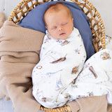 Newborn baby swaddled in a patterned blanket, lying in a wicker basket with a blue cushion.