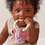 Child with a teething ring featuring butterfly designs on a neutral background