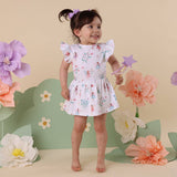 Young girl in a floral dress standing in front of large flowers with a pink background