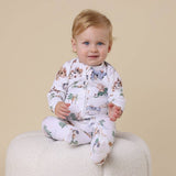 Baby wearing a white onesie with animal prints sitting on a beige surface.