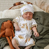 A sleeping newborn baby wearing a white short-sleeve footless onesie with a beige bunny print and a matching white beanie hat with a 'Sigh of Happiness' tag, resting on a dark green blanket next to an orange plush bunny toy.