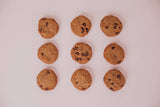 Nine chocolate chip cookies arranged in a 3x3 grid on a light pink background