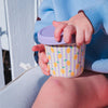 Child's hand holding a colorful mug with a striped pattern and lemon design.