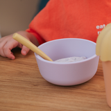 Child's hand holding a spoon over a bowl of food on a wooden table