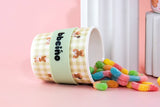 Colorful gummy bears spilling out of a 'babcino' cup on a pink background