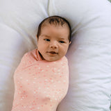Baby swaddled in a pink blanket with white polka dots on a white pillow