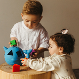 Two children playing with toys on a wooden table against a neutral background