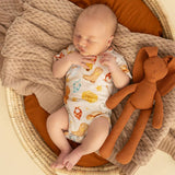 A sleeping newborn baby wearing a white footprints onesie, lying in a woven basket with a knit blanket and an orange plush bunny toy.