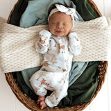 Newborn baby in a wicker basket with green and beige blankets, wearing a deer-themed onesie and headband.