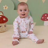 Baby wearing a white outfit with animal prints sitting on a beige surface with a colorful mushroom-themed background.