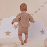 Baby in a beige outfit standing in front of a cloud and star wall decoration.