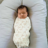 Newborn baby swaddled in a white blanket with bow patterns, lying on a soft surface.