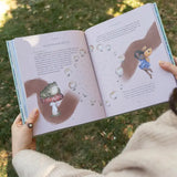 Person holding a book with illustrations of animals and bubbles on a grassy background