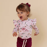 Child wearing a floral long-sleeve shirt and maroon pants with a bow on a beige background