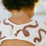 Close-up of a child wearing a white outfit with brown patterns on a blurred background