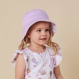 A young child wearing a light purple/lavender wide-brim sun hat with a chin strap and a white mermaid-print dress, set against a solid beige studio background.