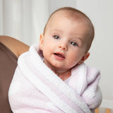 Baby wrapped in a pink towel sitting on a brown surface