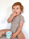 Child in a striped shirt holding a cup against a plain background