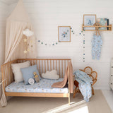 Nursery room with wooden crib, decorative pillows, and a shelf with baby clothes.