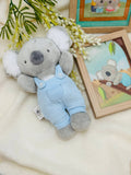 Plush toy koala in overalls on a soft surface with decorative elements.
