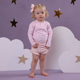 Young child in pink outfit standing against a purple background with star and cloud decorations