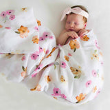 Newborn baby wrapped in a floral blanket with a matching headband on a light background