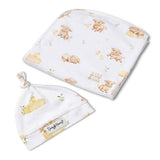 A baby gift set featuring a soft white muslin swaddle blanket and matching knotted beanie hat, both printed with a cute watercolor-style pattern of baby pigs, chicks, and a small fence. The beanie has a visible 'Simply Honey' brand label.