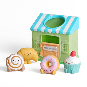 Toy bakery set with a green and blue striped roof, featuring a donut, cupcake, and other items on a white background.