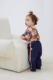 Child wearing a colorful patterned shirt and navy pants with a red and white striped tie, standing on a white floor.