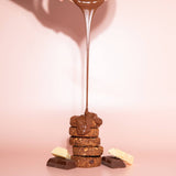 Chocolate being drizzled over a stack of cookies on a pink background