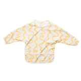A long-sleeve baby bib with a cream base and a mustard yellow wavy line pattern, laid flat on a white background.