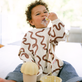 Child wearing a brown wavy patterned shirt eating a snack indoors.