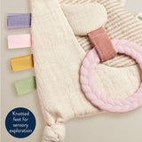 Baby soft toy with knotted feet and colorful ribbons on a light background