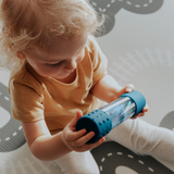 Child holding a blue cylindrical toy on a patterned rug