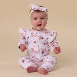 Baby in a floral onesie with ruffled sleeves and legs on a beige background