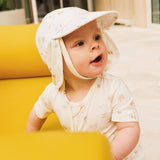 Baby wearing a patterned sun hat sitting on a yellow surface.