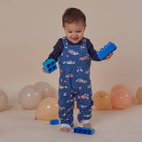Child in blue overalls with car pattern holding blue blocks against a beige background with balloons.
