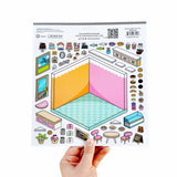 A hand holds a sheet of Bricks by Bricks DIY Kit sticker templates featuring a colorful isometric room design with pink and yellow walls, a teal floor, and various kitchen and decor accessories.