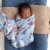 Newborn baby swaddled in a blanket with vehicle patterns, lying on a textured surface.