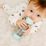 Baby holding a glittery bottle with a light blue lid on a soft surface