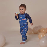 Child wearing a blue romper with car pattern, holding a toy, surrounded by balloons on a beige background
