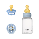 BIBS baby bottle and pacifier set on a white background, featuring a clear bottle with a light blue collar and yellow nipple, alongside a light blue pacifier with a yellow nipple.