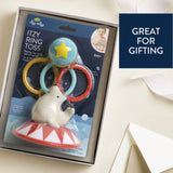 A boxed baby toy set labeled 'Itzy Ring Toss' by ddy nnnn, shown in its packaging on a light cream background with a 'Great for Gifting' promotional badge. The product includes a white elephant-shaped rattle on a red-and-white circus base with three hanging rings in yellow, blue, and red, plus a blue ball with a yellow star.