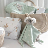 Baby comfort blanket with koala design next to a basket and wrapped gift on a light surface.