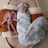 Newborn baby swaddled in a blanket with animal patterns, lying in a basket with a pink stuffed toy.