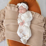 Newborn baby in a white outfit with floral patterns, lying on a textured beige blanket.